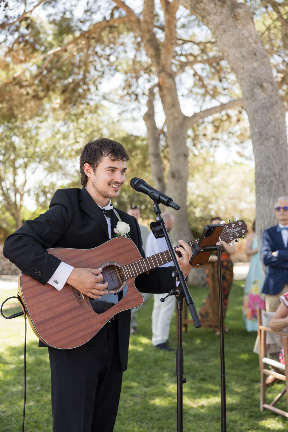 Genie playing acoustic guitar at an outdoor wedding reception