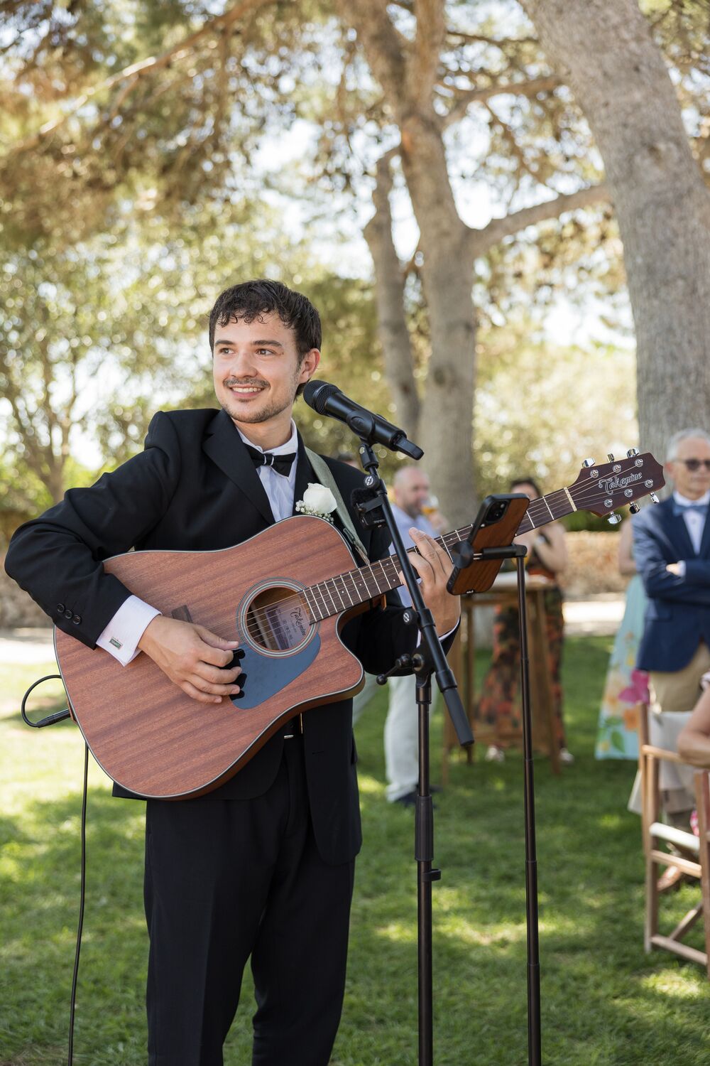 Genie performing in black tie with guests watching behind him